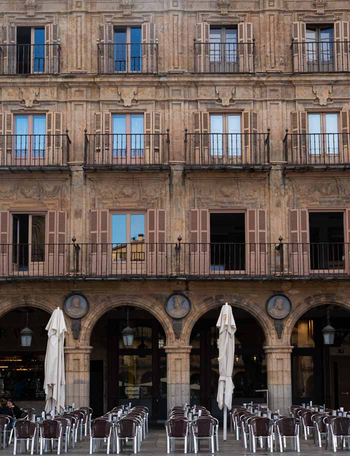 Fachada en la Plaza Mayor de Salamanca con una terraza y al fondo medallones de personajes históricos